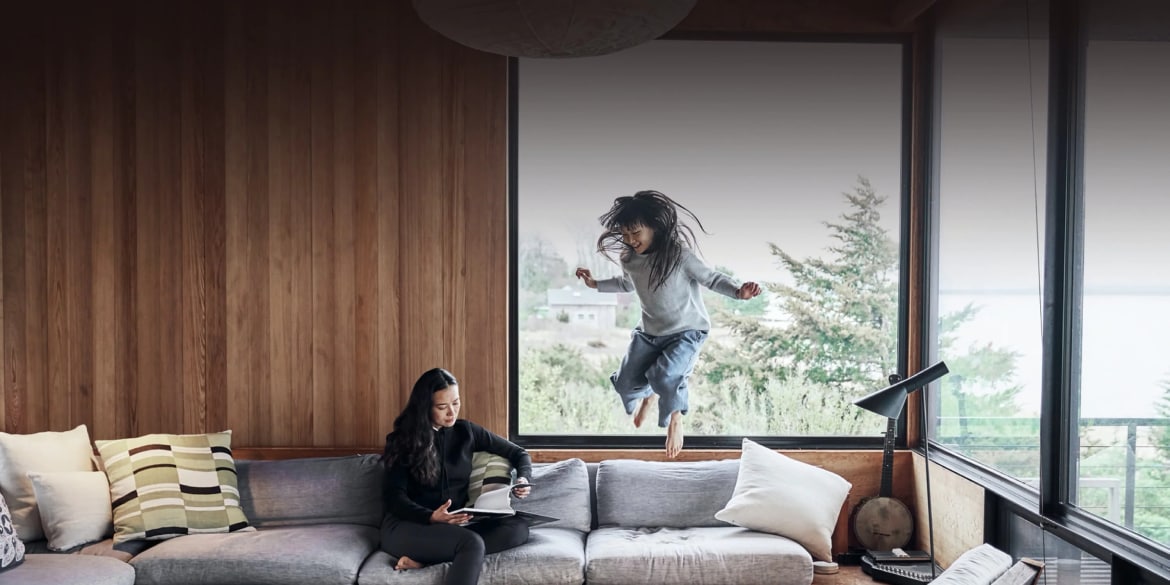 Image of woman sitting on a couch while young girl jumps off couch
